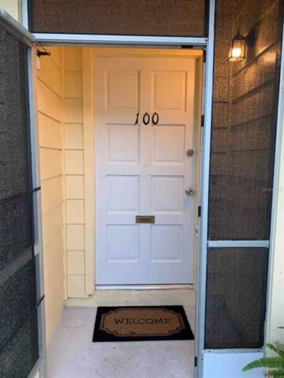 A white front door with the number 100 is framed by a screen door — 1144 VILLA LANE UNIT 100, APOPKA, FL