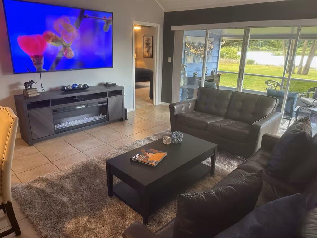 A living room with tile floors, a large television, dark furniture, and a sliding glass door — 1144 VILLA LANE UNIT 100, APOPKA, FL