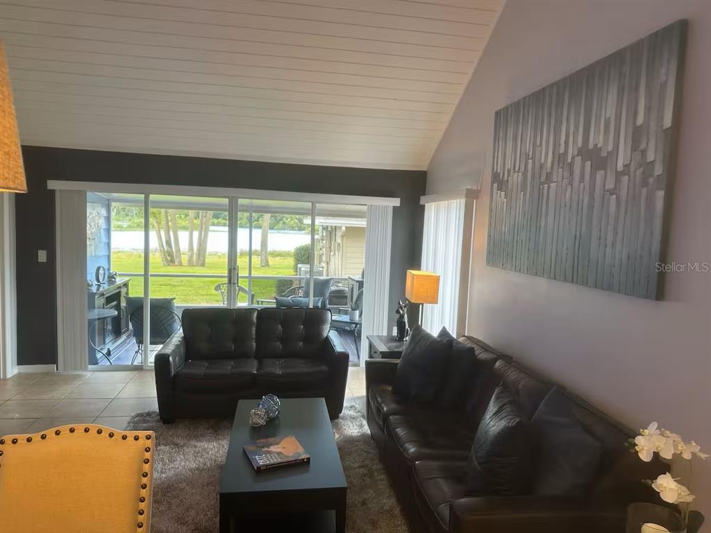 A living room features dark leather sofas, a coffee table, and sliding doors overlooking a lake — 1144 VILLA LANE UNIT 100, APOPKA, FL