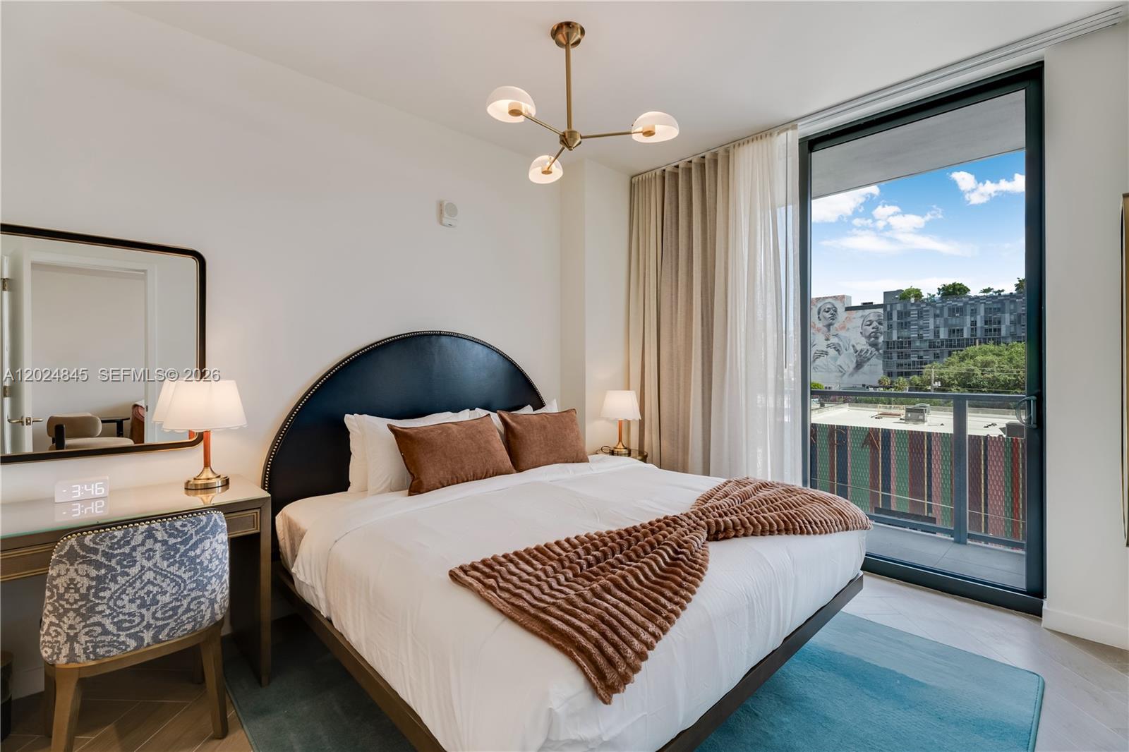 A bedroom features a dark arched headboard, a textured throw blanket, and a balcony view — 2700 NW 2nd Ave # 309, Miami FL 33127, MIAMI, FL