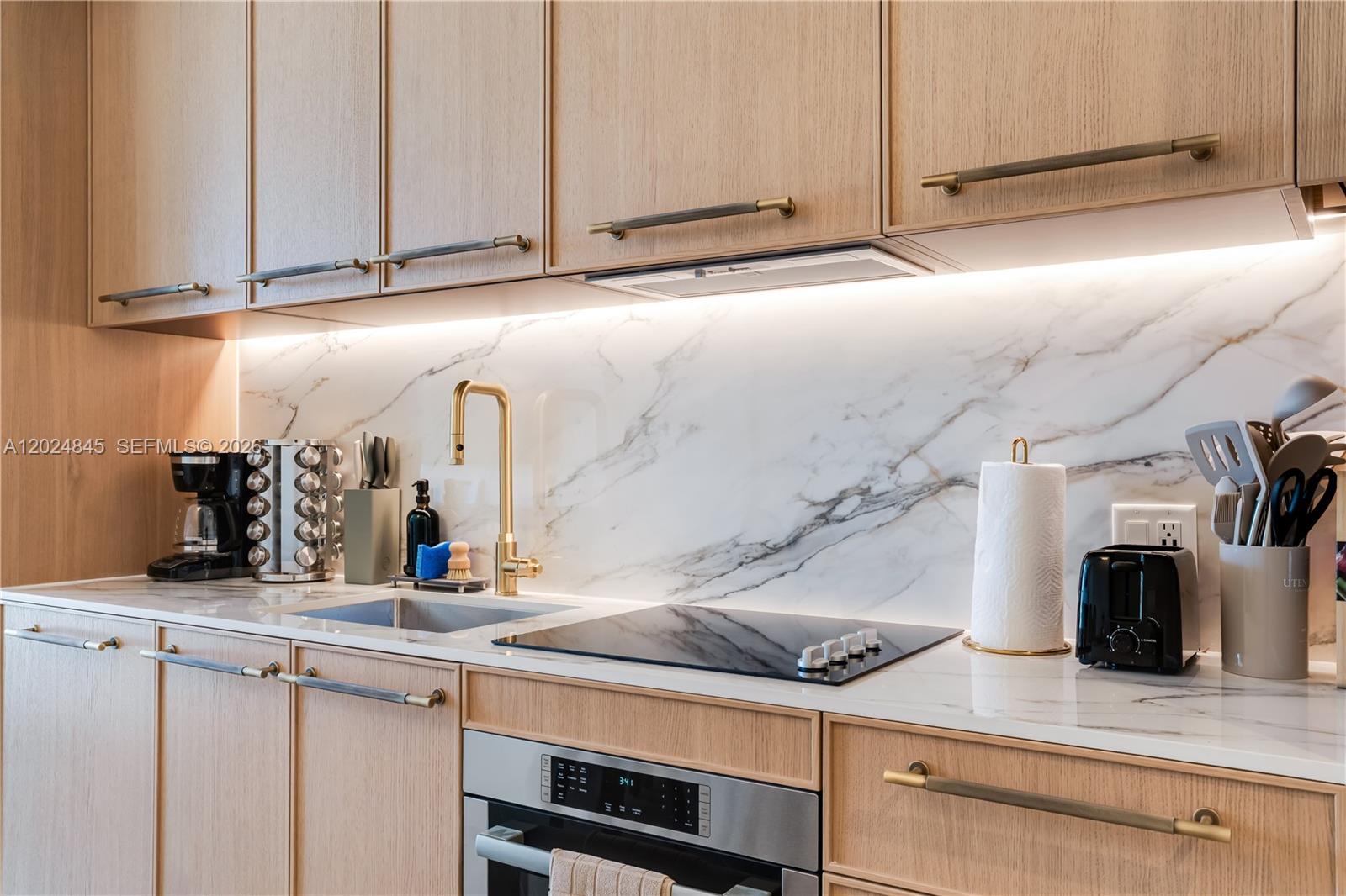 A modern kitchen features light wood cabinets, a marble backsplash, and a gold faucet — 2700 NW 2nd Ave # 309, Miami FL 33127, MIAMI, FL