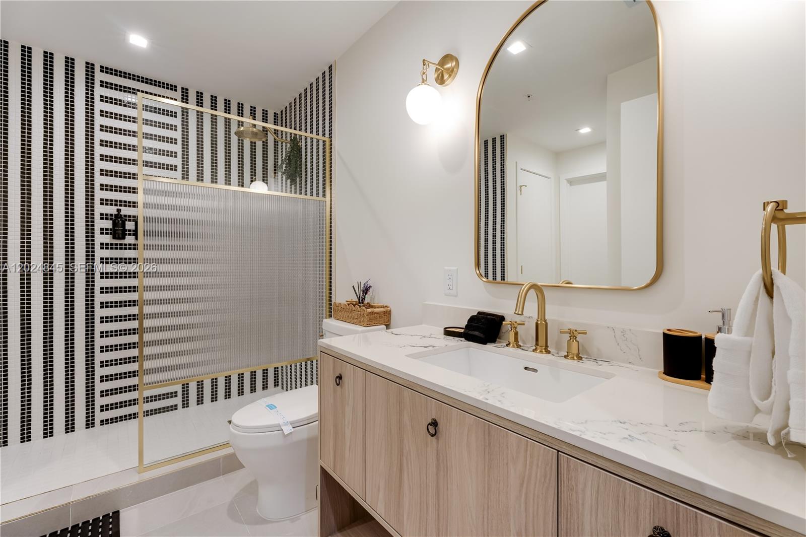 A modern bathroom features a striped tile shower, gold fixtures, and a light wood vanity — 2700 NW 2nd Ave # 309, Miami FL 33127, MIAMI, FL