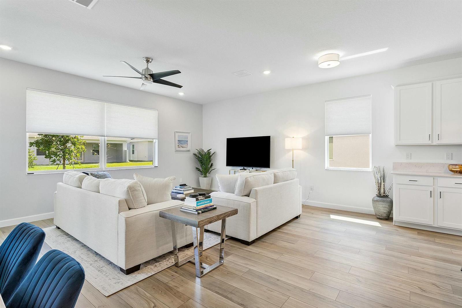 A bright living room features light wood flooring, white sofas, and a ceiling fan — 13404 Brotherhood Way, Delray Beach FL 33484, DELRAY BEACH, FL