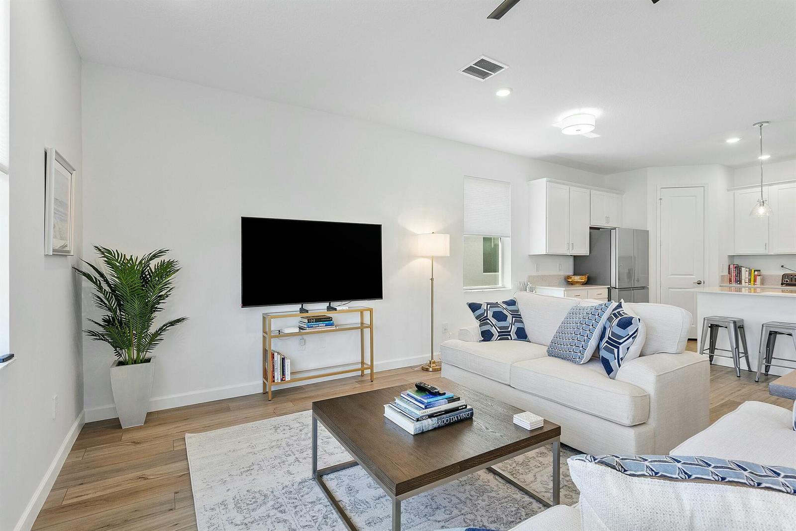 A living room features a wall-mounted television, a sofa, and an open-concept kitchen — 13404 Brotherhood Way, Delray Beach FL 33484, DELRAY BEACH, FL