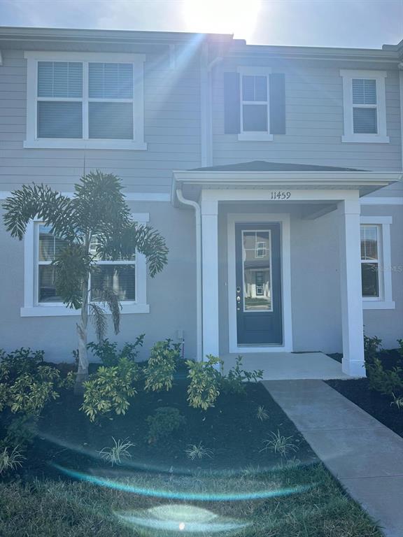 The exterior of a two-story townhouse features light gray siding, a covered entryway, and landscaping — 11459 SUNSAIL AVENUE, ORLANDO, FL
