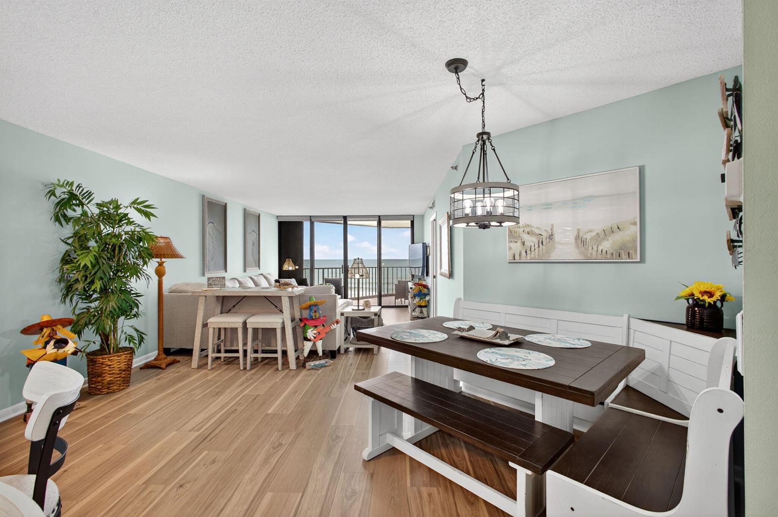 A dining area with a wooden table and bench seating sits next to a living room — 9650 S Ocean Drive # 302, Jensen Beach FL 34957, JENSEN BEACH, FL