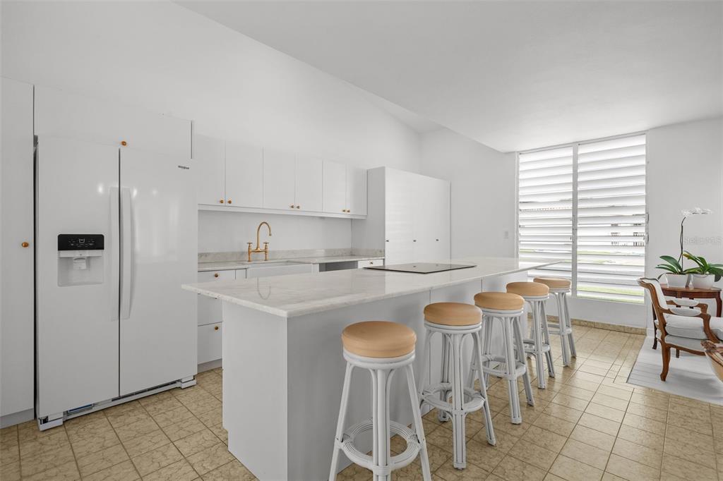 A white kitchen features a marble-topped island with bar stools and tile flooring — AF7 Villa Franca BARCELONA ST, HUMACAO, PR