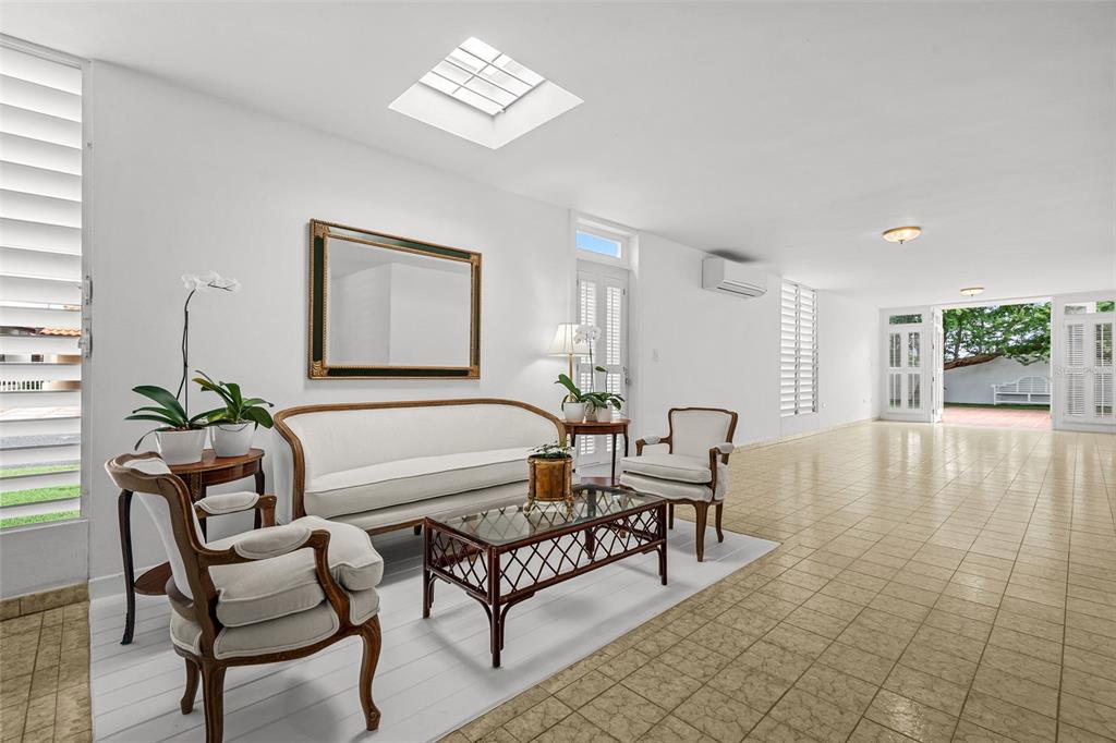 A bright living room features a white sofa, patterned chairs, a glass coffee table, and skylight — AF7 Villa Franca BARCELONA ST, HUMACAO, PR