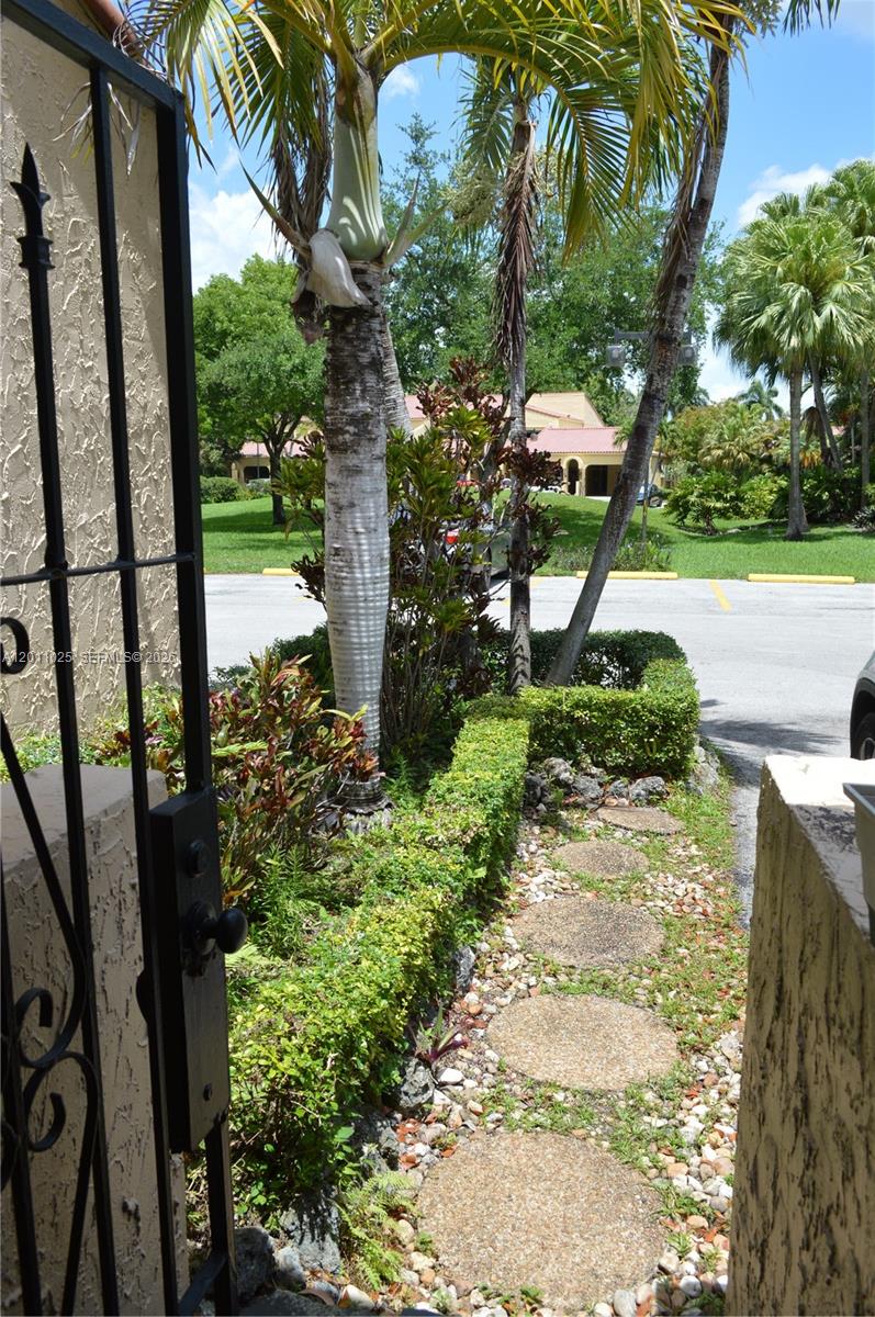 A stone path leads through a garden gate toward a parking lot and tropical landscaping — 3932 Estepona Ave, Doral FL 33178, DORAL, FL