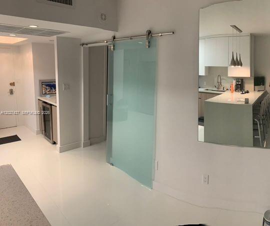 A frosted glass sliding door separates a hallway from a modern kitchen with white cabinetry — 100 Lincoln Rd # 1535, Miami Beach FL 33139, MIAMI BEACH, FL