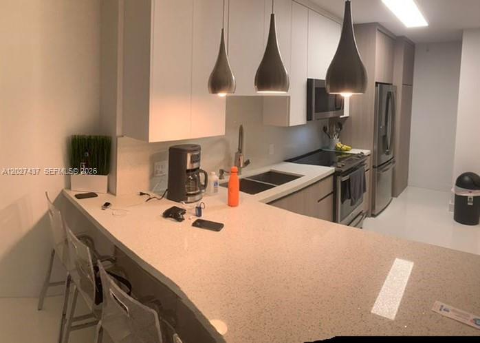 A modern kitchen features white cabinets, a quartz breakfast bar, and three pendant lights — 100 Lincoln Rd # 1535, Miami Beach FL 33139, MIAMI BEACH, FL