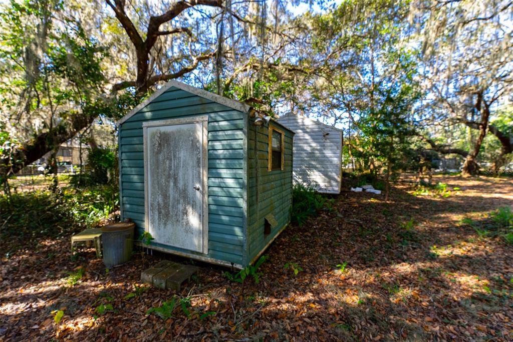 A weathered teal shed with a white door sits in a wooded yard — 24971 NE 135TH STREET, SALT SPRINGS, FL