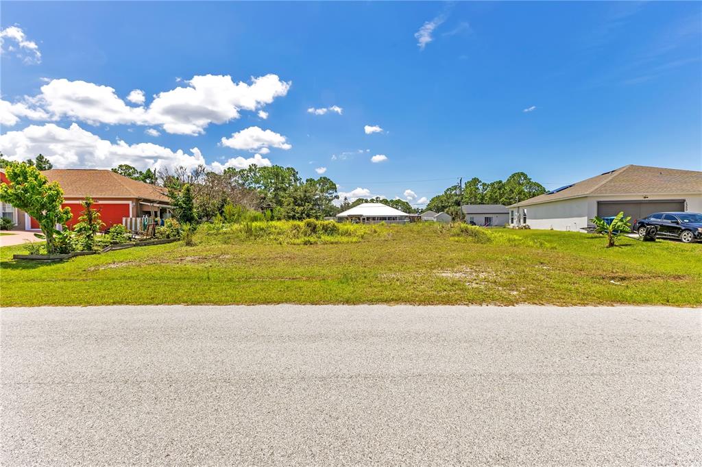 A vacant, grassy residential lot sits between two existing houses under a blue sky — 1358 TORDIRA STREET SE, PALM BAY, FL