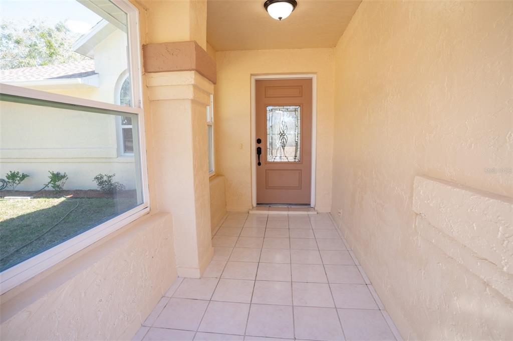A covered entryway features a tan front door, tiled flooring, and a large side window — 12989 NW HIGHWAY 225, REDDICK, FL