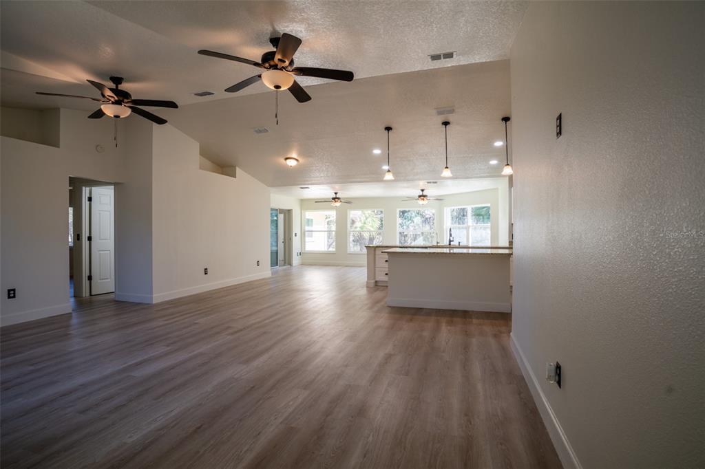 An open-concept living area features light wood-look flooring, vaulted ceilings with fans, and a kitchen island — 12989 NW HIGHWAY 225, REDDICK, FL