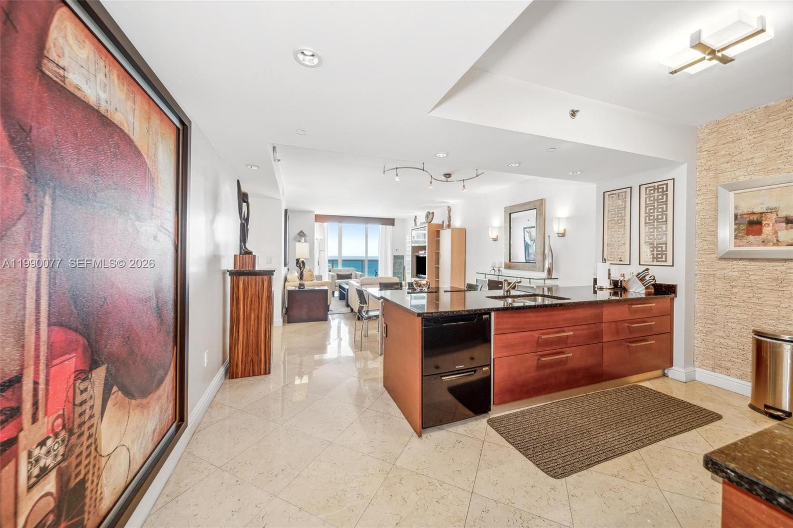 A modern kitchen with wood cabinets and a granite island overlooks an open living area — 1830 S Ocean Dr # 3111, Hallandale Beach FL 33009, HALLANDALE BEACH, FL