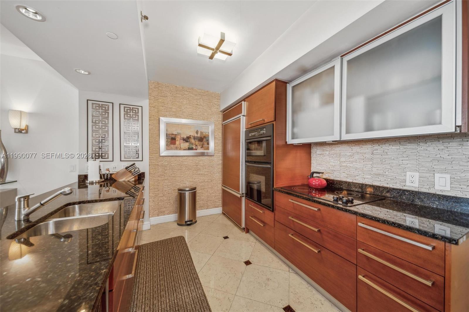 A modern kitchen features wood cabinetry, dark granite countertops, stainless steel appliances, and tiled flooring — 1830 S Ocean Dr # 3111, Hallandale Beach FL 33009, HALLANDALE BEACH, FL