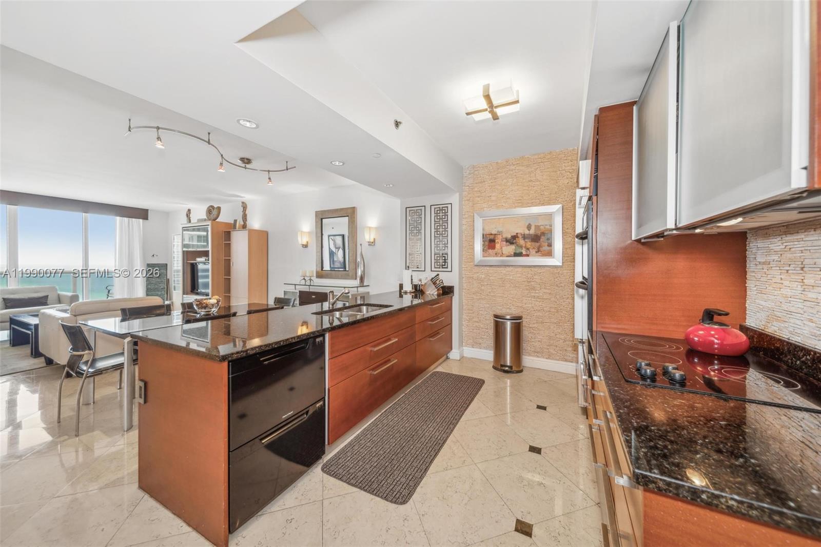 A modern kitchen features dark granite countertops, wood cabinetry, and a large central island — 1830 S Ocean Dr # 3111, Hallandale Beach FL 33009, HALLANDALE BEACH, FL