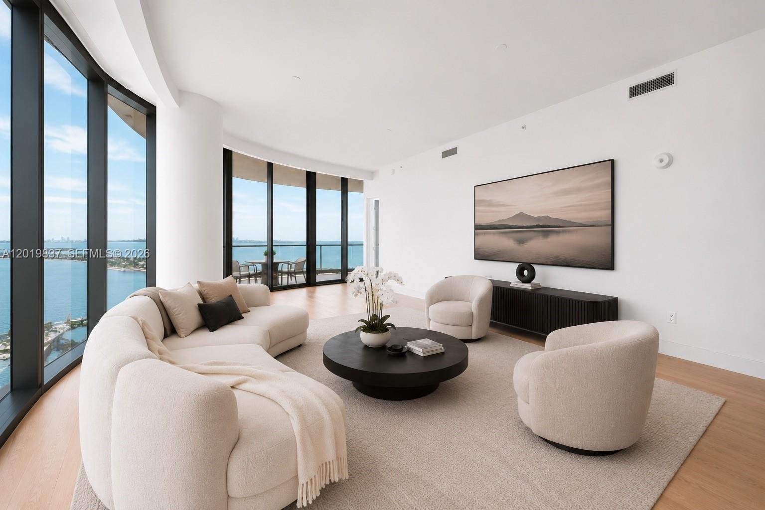 A modern living room features a curved sofa, two armchairs, and floor-to-ceiling windows overlooking water — 175 SE 25 Rd # 801, Miami FL 33129, MIAMI, FL
