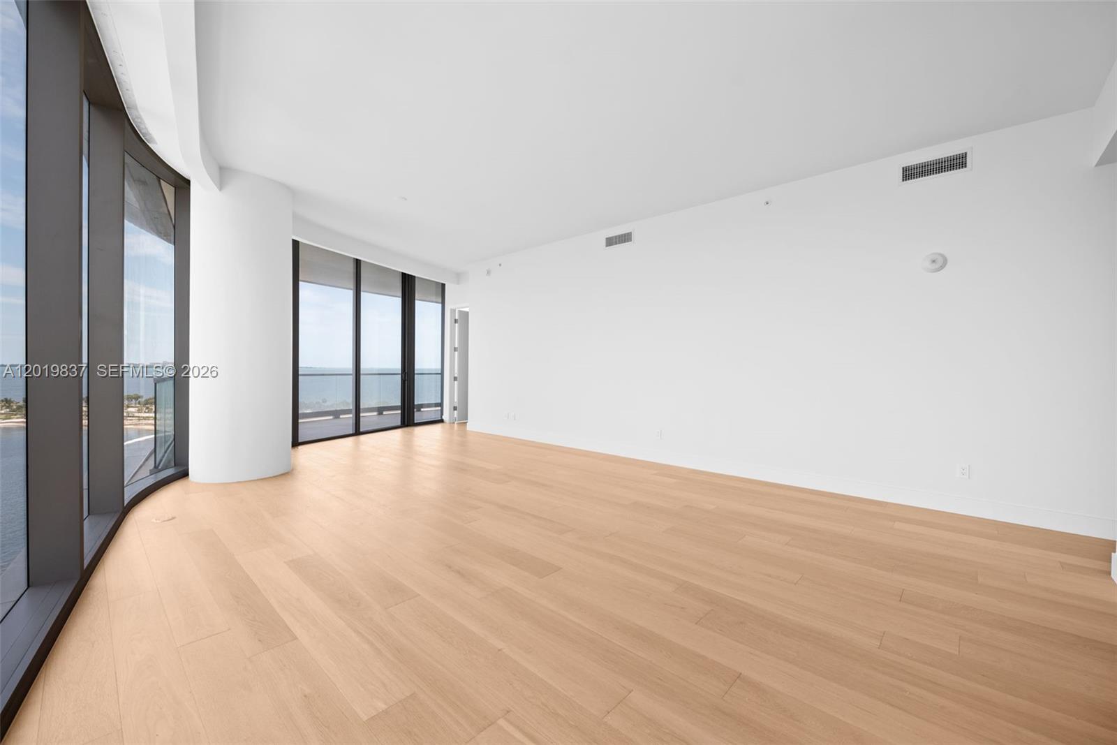 An empty room features light wood flooring, white walls, and floor-to-ceiling windows with water views — 175 SE 25 Rd # 801, Miami FL 33129, MIAMI, FL