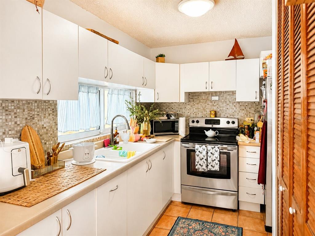 A kitchen with white cabinets, stainless steel appliances, a tiled backsplash, and terracotta floor tiles — PRINCIPAL CASA DEL MAR II UNIT 2705, RIO GRANDE, PR