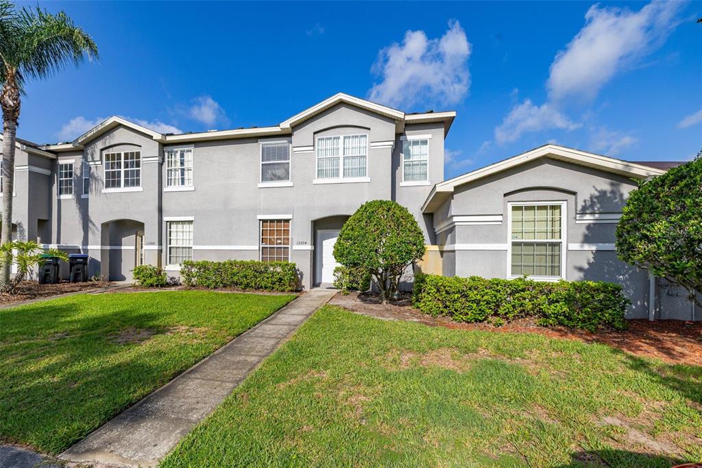 A two-story gray stucco townhouse features a front walkway, green lawn, and multiple windows — 13304 SUMMERTON DRIVE, ORLANDO, FL