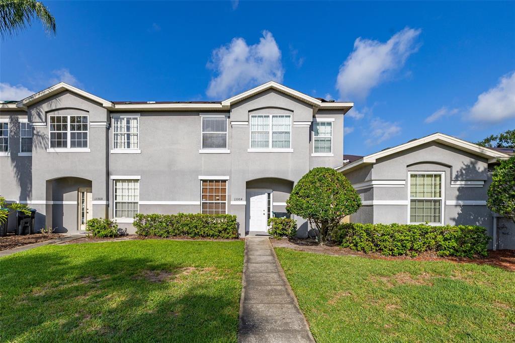 A two-story gray townhouse features a front walkway, green lawn, and manicured landscaping — 13304 SUMMERTON DRIVE, ORLANDO, FL