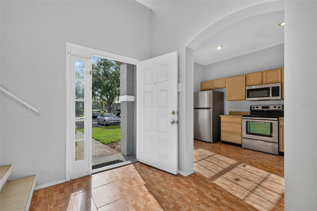An entryway with tile flooring leads to an open kitchen featuring light wood cabinets — 13304 SUMMERTON DRIVE, ORLANDO, FL