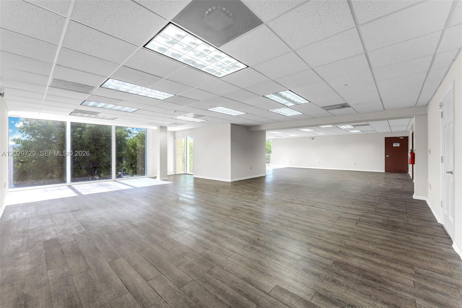 An empty office space features wood-look flooring, a drop ceiling with recessed lighting, and large windows — 2100 NW 102nd Pl, Doral FL 33172, DORAL, FL