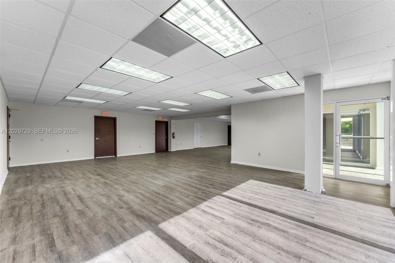 An empty commercial office space with wood-look flooring, drop ceilings, and a glass entry door — 2100 NW 102nd Pl, Doral FL 33172, DORAL, FL