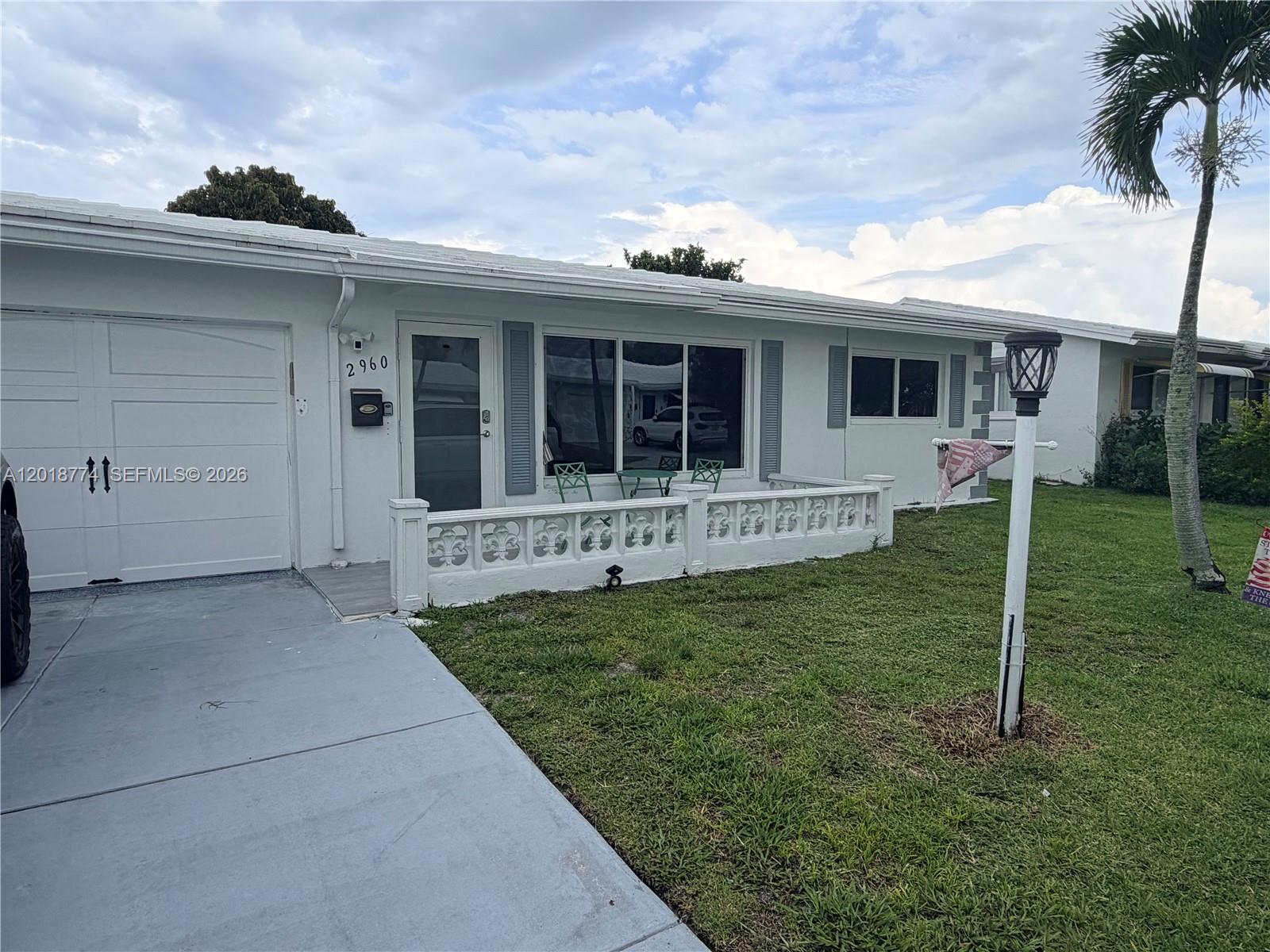 A white single-story house features a garage, a small front patio, and a palm tree — 2960 NW 1st Dr, Pompano Beach FL 33064, POMPANO BEACH, FL