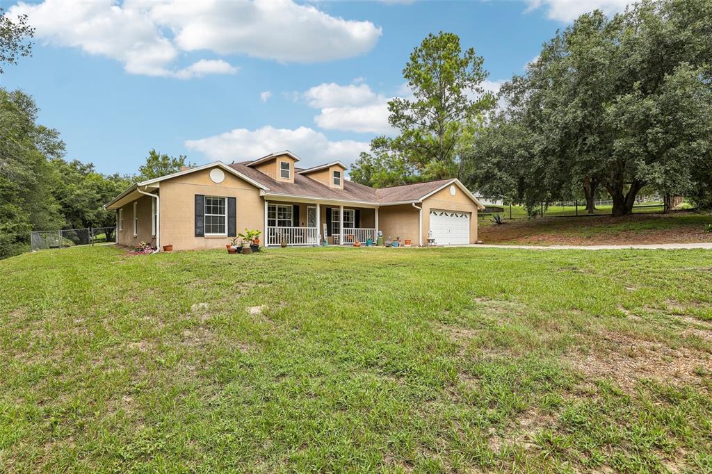 A tan, single-story house with a front porch, dormer windows, and an attached garage — 30733 BUTTERCUP LANE, MOUNT DORA, FL