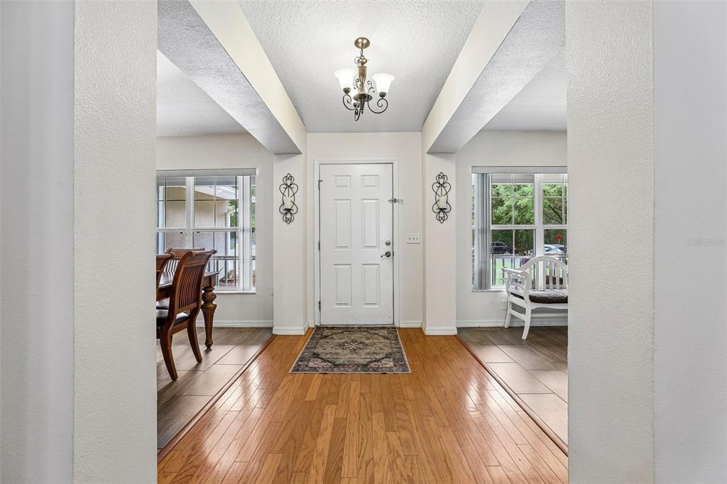 A foyer with hardwood floors leads to a white front door under a chandelier — 30733 BUTTERCUP LANE, MOUNT DORA, FL