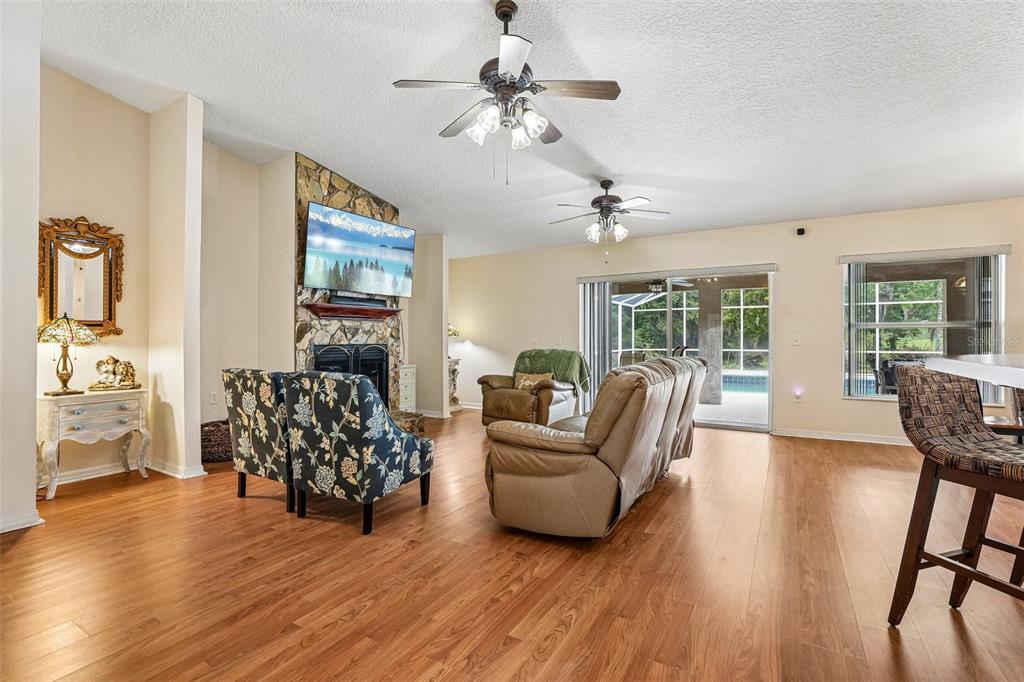 A living room with wood flooring, a stone fireplace, two ceiling fans, and sliding glass doors — 30733 BUTTERCUP LANE, MOUNT DORA, FL