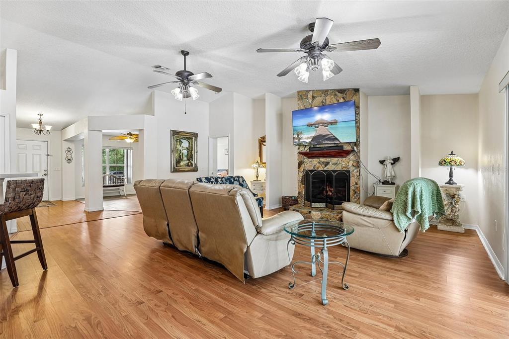 A living room features wood flooring, a stone fireplace with a television, and two ceiling fans — 30733 BUTTERCUP LANE, MOUNT DORA, FL