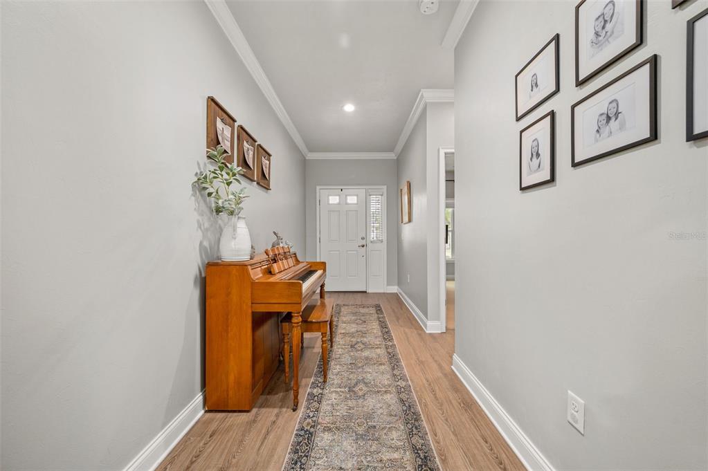 A hallway with light gray walls, wood-look flooring, a piano, and framed wall art — 16635 NW 193RD TERRACE, HIGH SPRINGS, FL