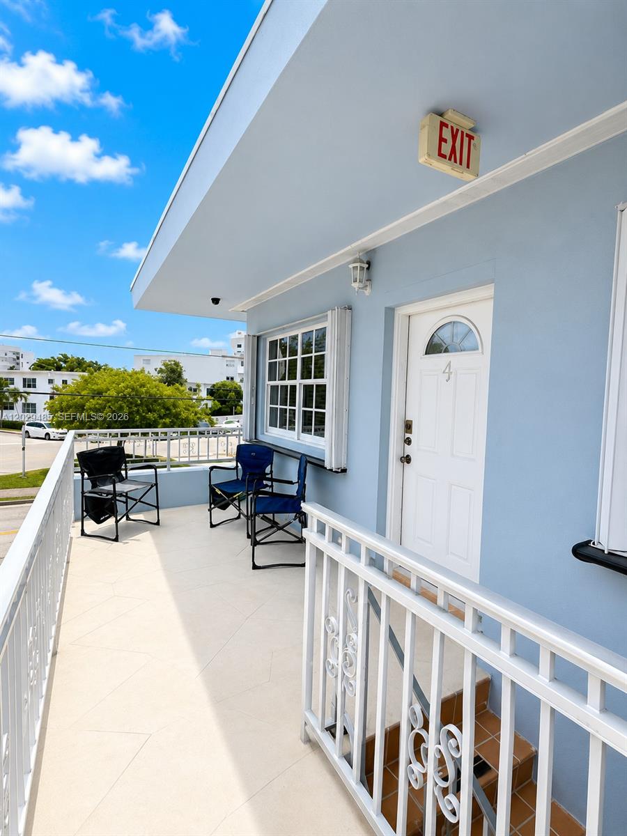 A light blue exterior balcony features a white door, two folding chairs, and metal railings — MIAMI BEACH, FL