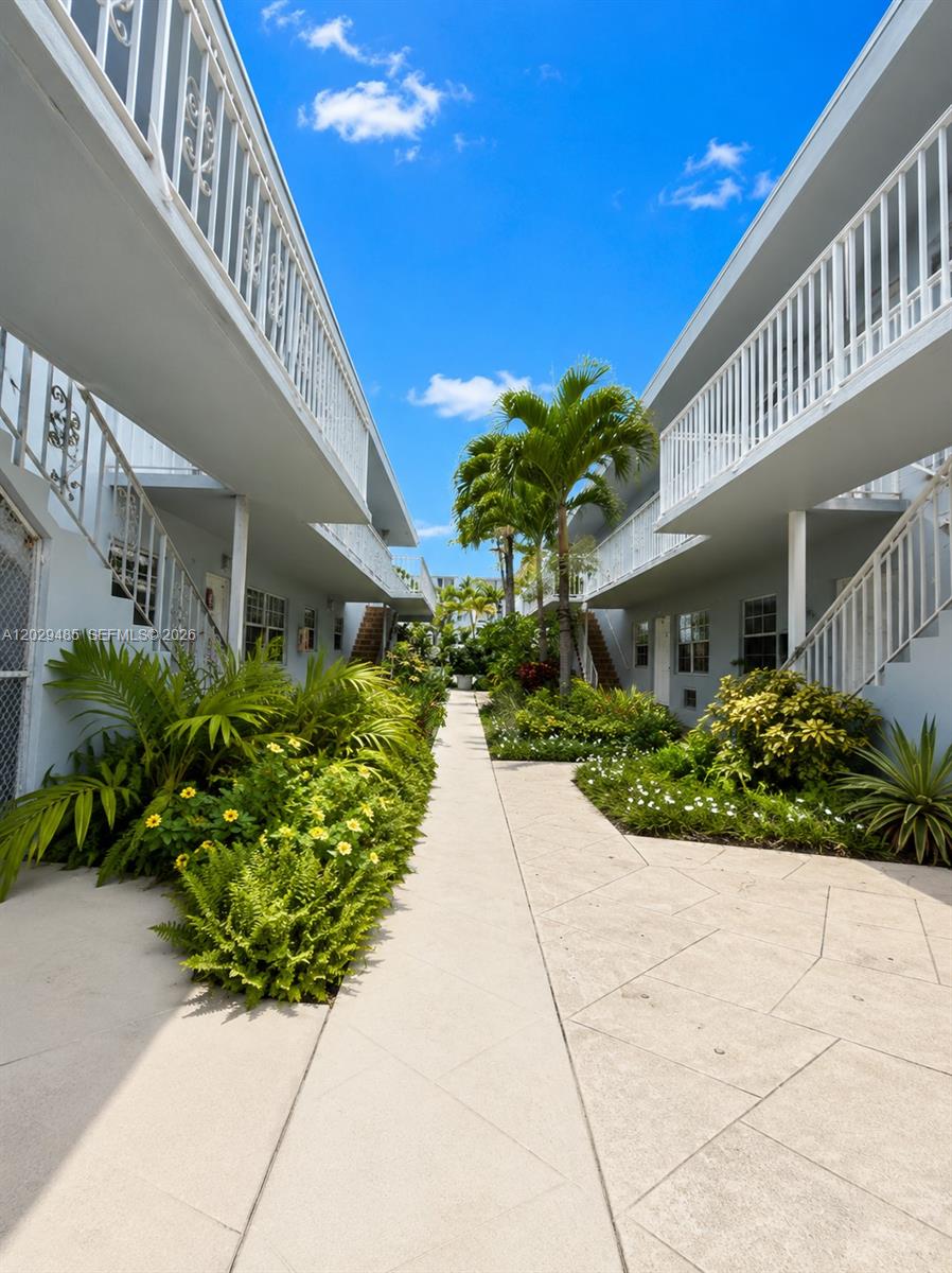A paved walkway leads between two two-story apartment buildings with white railings and landscaping — MIAMI BEACH, FL