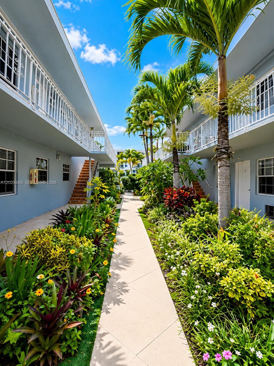 A paved walkway leads between two light blue apartment buildings surrounded by lush tropical landscaping — MIAMI BEACH, FL