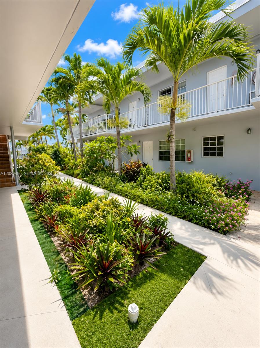 A two-story apartment building features a landscaped courtyard with palm trees and a walkway — MIAMI BEACH, FL
