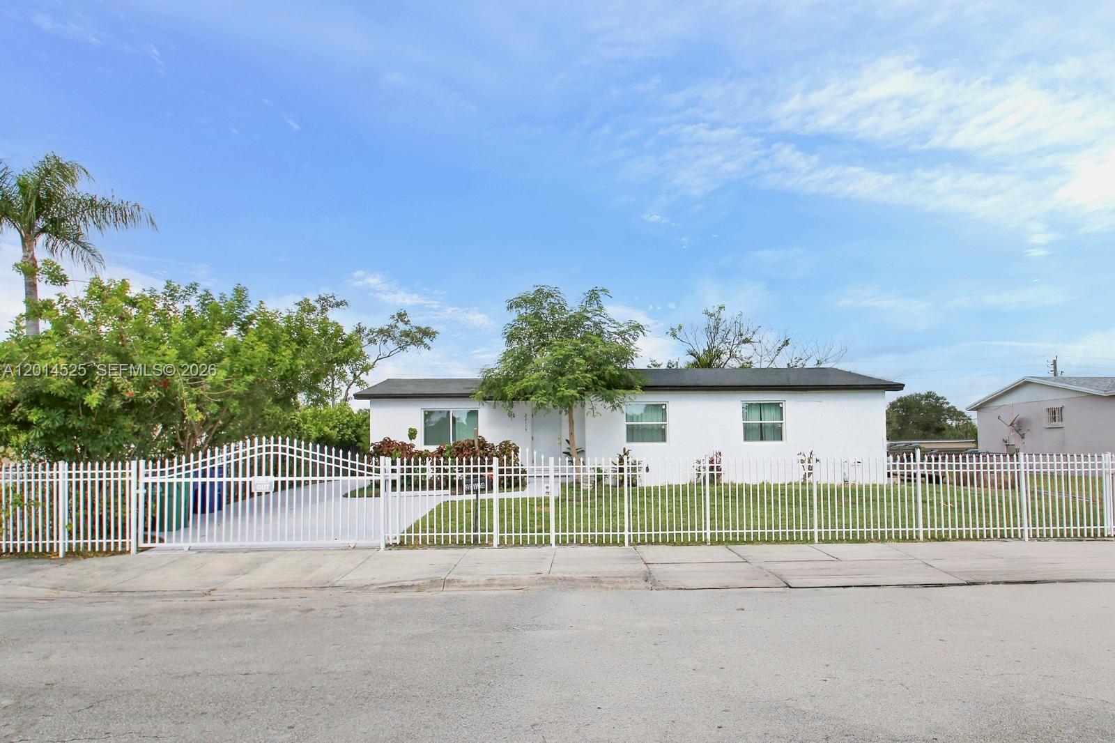 A white single-story house with a black roof sits behind a white metal fence — 22114 SW 113th Pl, Miami FL 33170, MIAMI, FL
