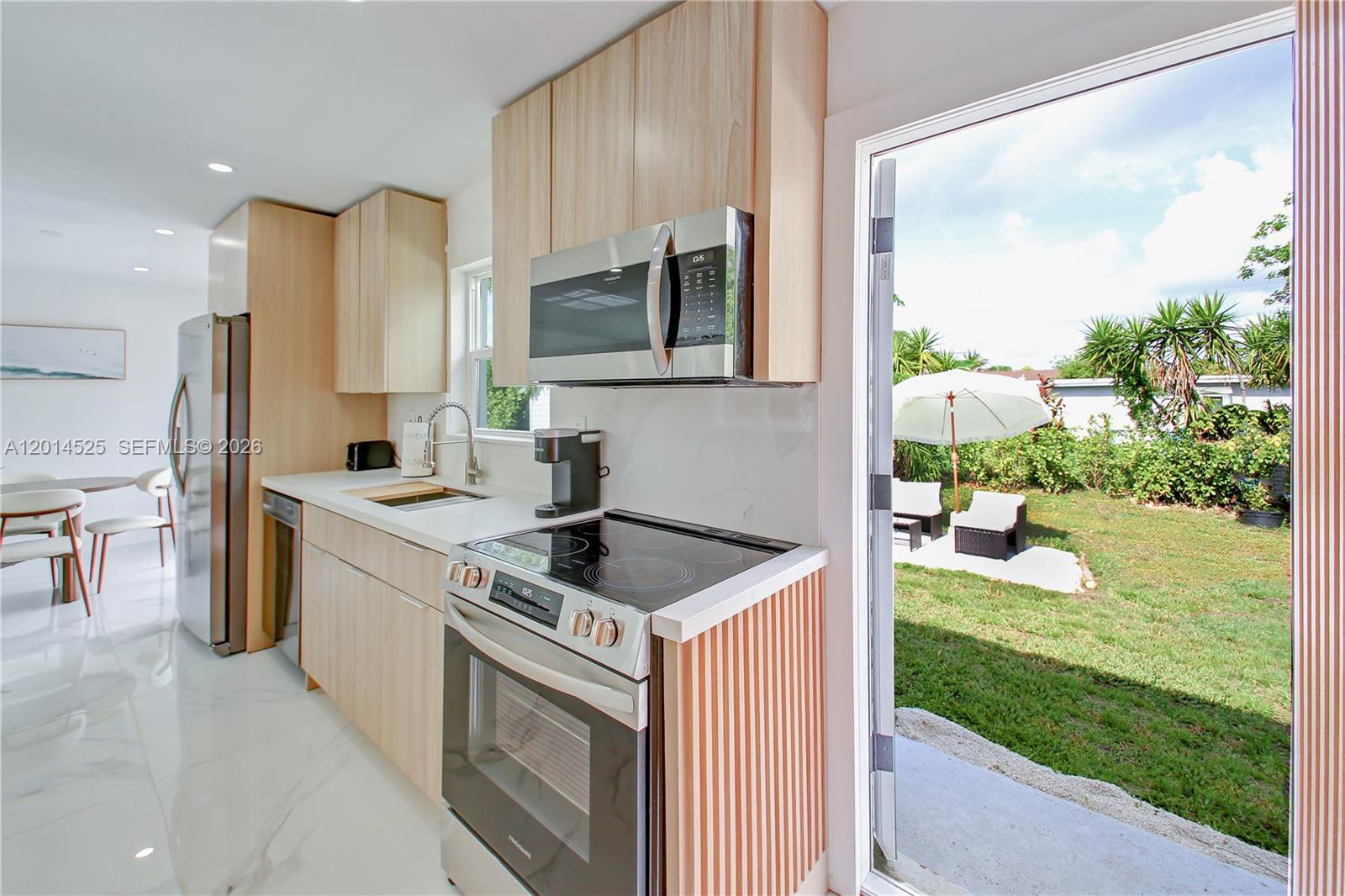A modern kitchen with light wood cabinets, stainless steel appliances, and a view of a backyard — 22114 SW 113th Pl, Miami FL 33170, MIAMI, FL