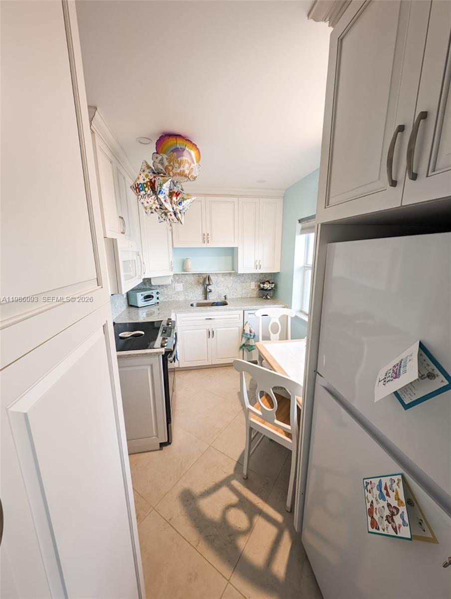 A kitchen features white cabinets, stainless steel appliances, a small dining table, and tile flooring — 1501 S Surf Rd # 21, Hollywood FL 33019, HOLLYWOOD, FL