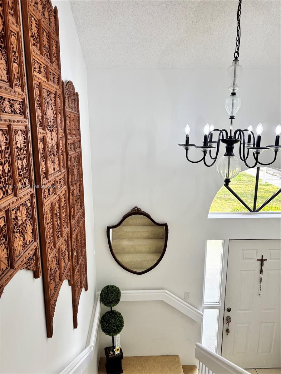 A high-ceilinged foyer features a chandelier, a wooden room divider, and a wall-mounted display case — 5258 Europa Dr # H, Boynton Beach FL 33437, BOYNTON BEACH, FL