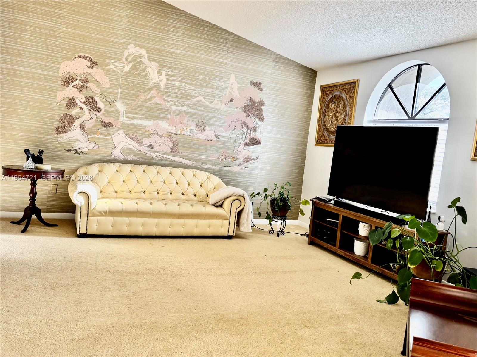 A living room features a tufted cream sofa, a large television, and a scenic wallpaper mural — 5258 Europa Dr # H, Boynton Beach FL 33437, BOYNTON BEACH, FL