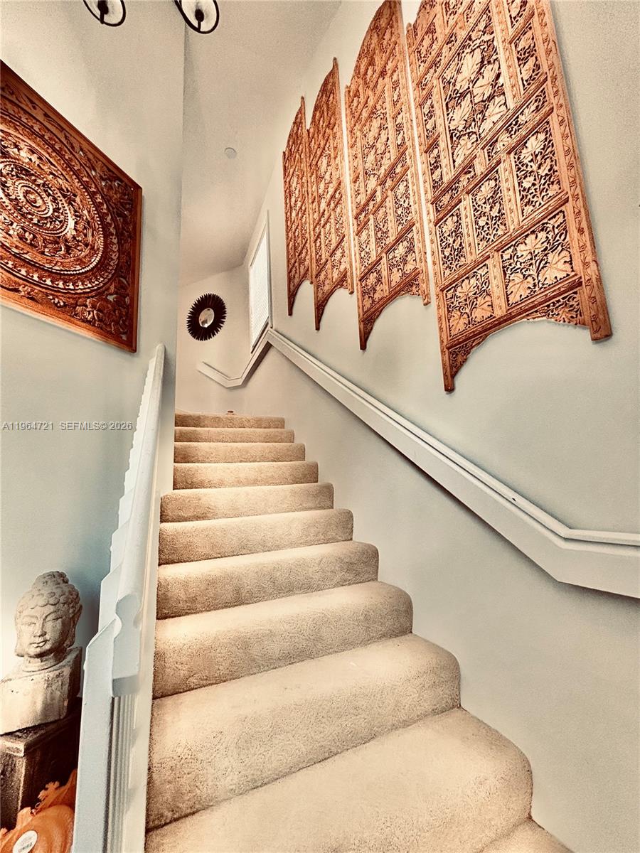A carpeted staircase features decorative carved wooden wall panels and a Buddha statue — 5258 Europa Dr # H, Boynton Beach FL 33437, BOYNTON BEACH, FL