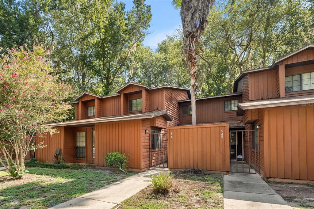 A two-story brown wood-sided townhouse exterior with a palm tree and a small front yard — 825 SW 55TH TERRACE, GAINESVILLE, FL