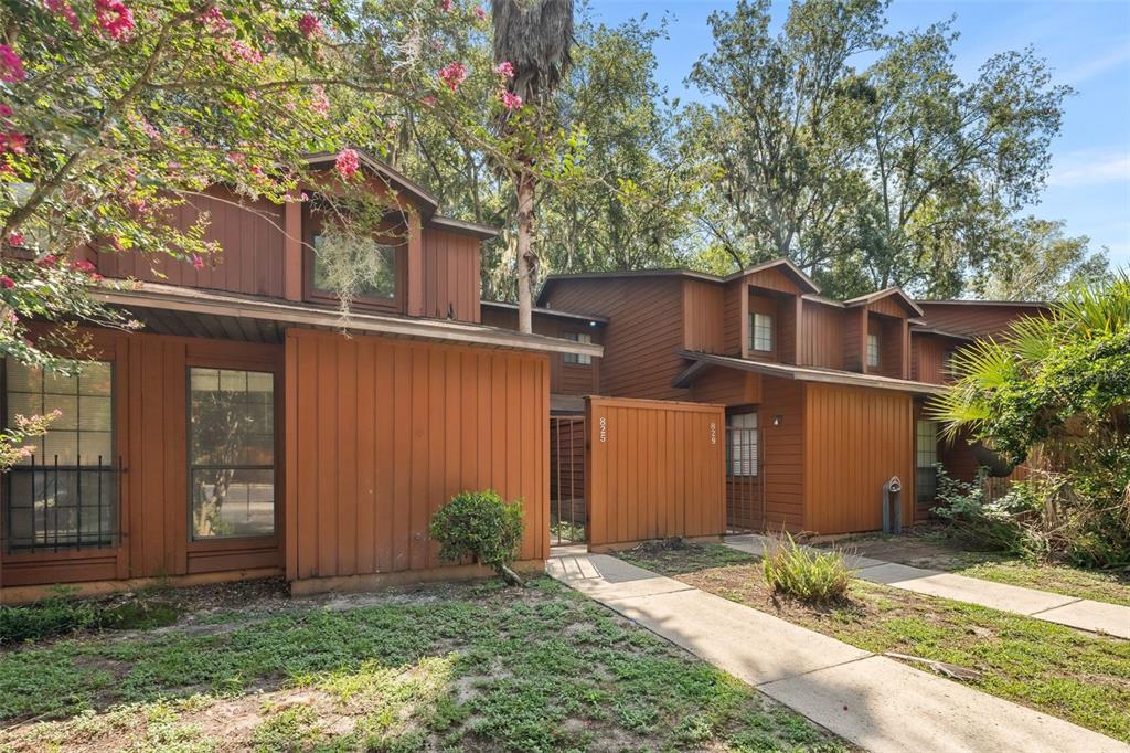 A two-story brown wood-sided townhouse exterior with a walkway and surrounding trees — 825 SW 55TH TERRACE, GAINESVILLE, FL