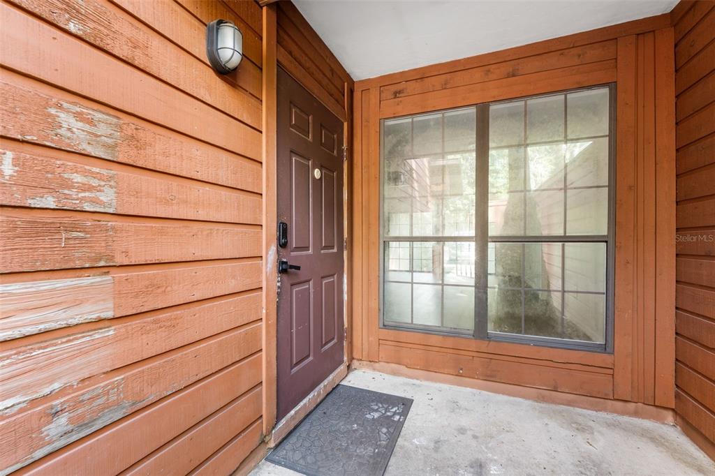 A brown front door and a large window are set into a wood-sided exterior wall — 825 SW 55TH TERRACE, GAINESVILLE, FL
