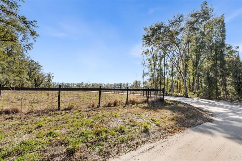 A dirt road runs alongside a fenced, grassy field bordered by tall trees — 17807 SW 83RD AVENUE, ARCHER, FL
